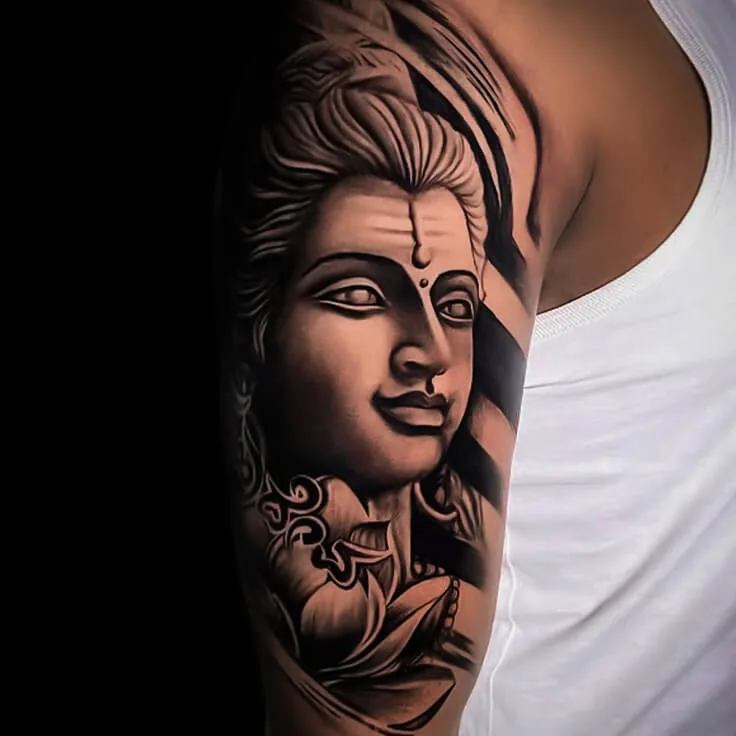 Black-and-grey Shiva upper-arm tattoo with calm portrait detail by Apex Tattooz