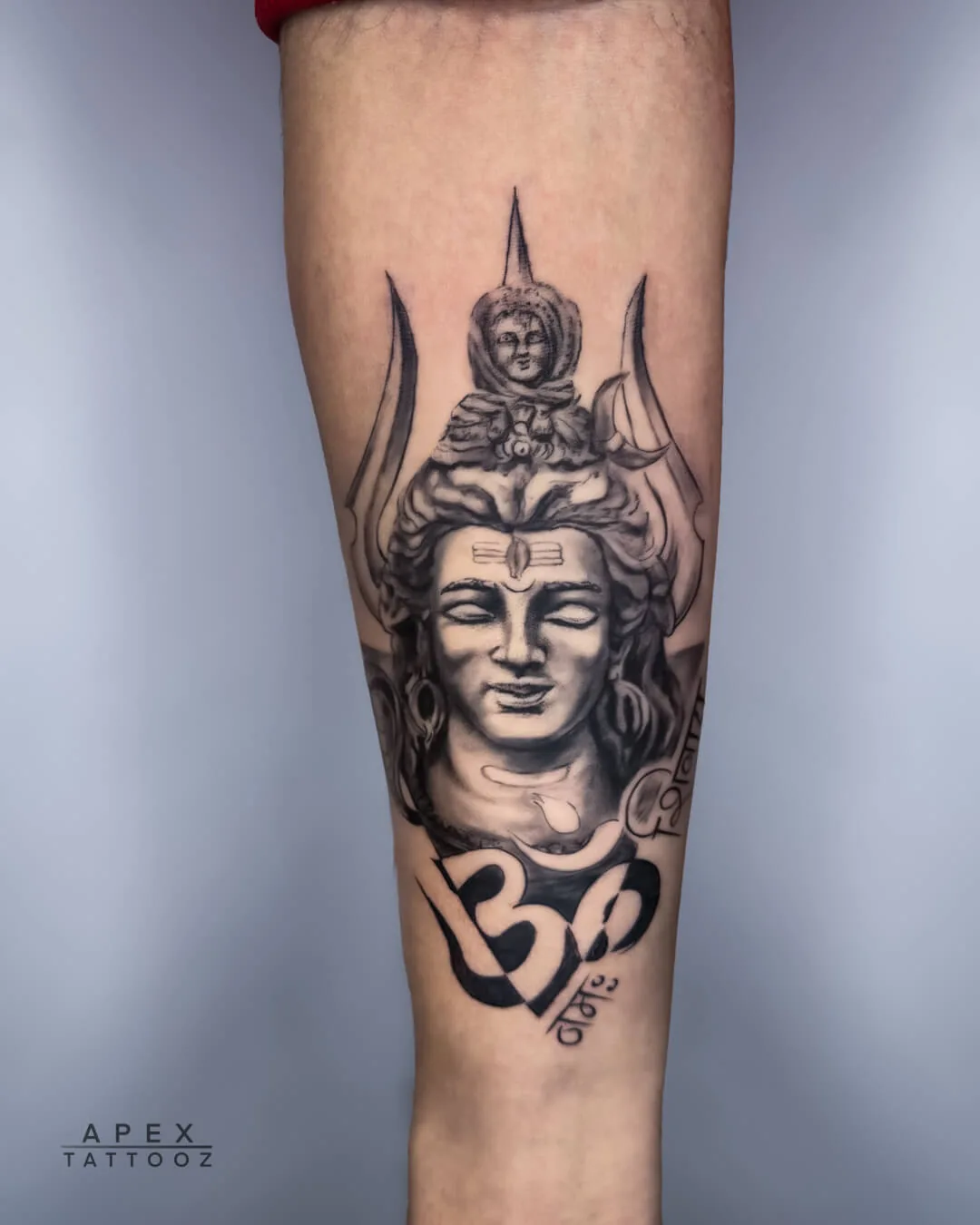 Shiva portrait and Om black-and-grey forearm tattoo by Apex Tattooz