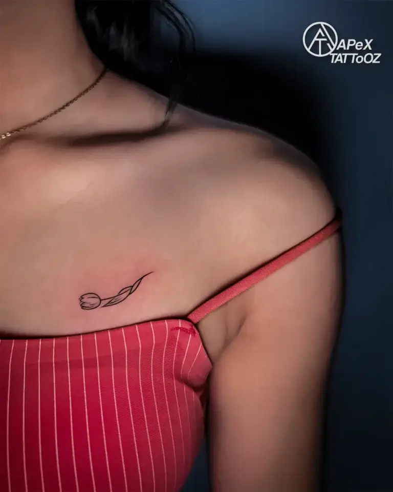 Small fine-line tulip tattoo on the upper back near the shoulder by Apex Tattooz