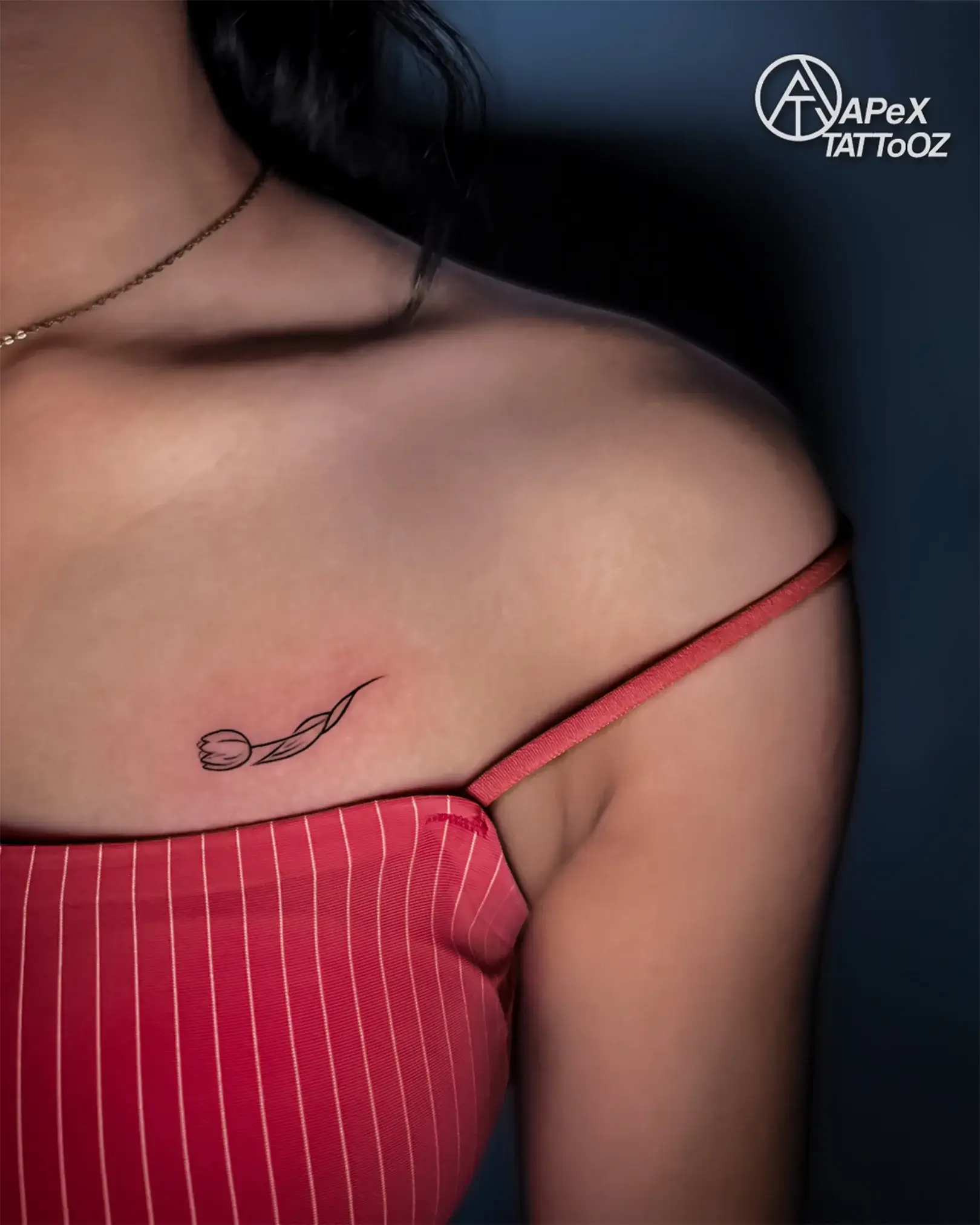 Small fine-line tulip tattoo on the upper back near the shoulder by Apex Tattooz