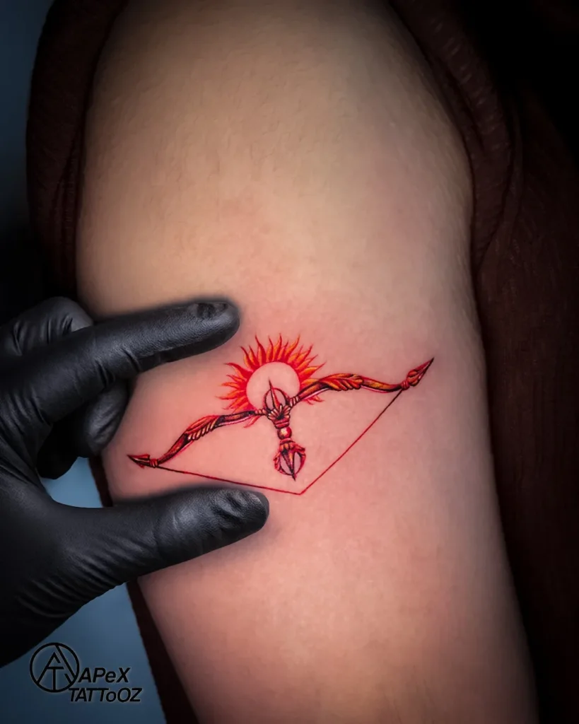Small upper-arm tattoo design with a colour bow, arrow and sun by Apex Tattooz Delhi