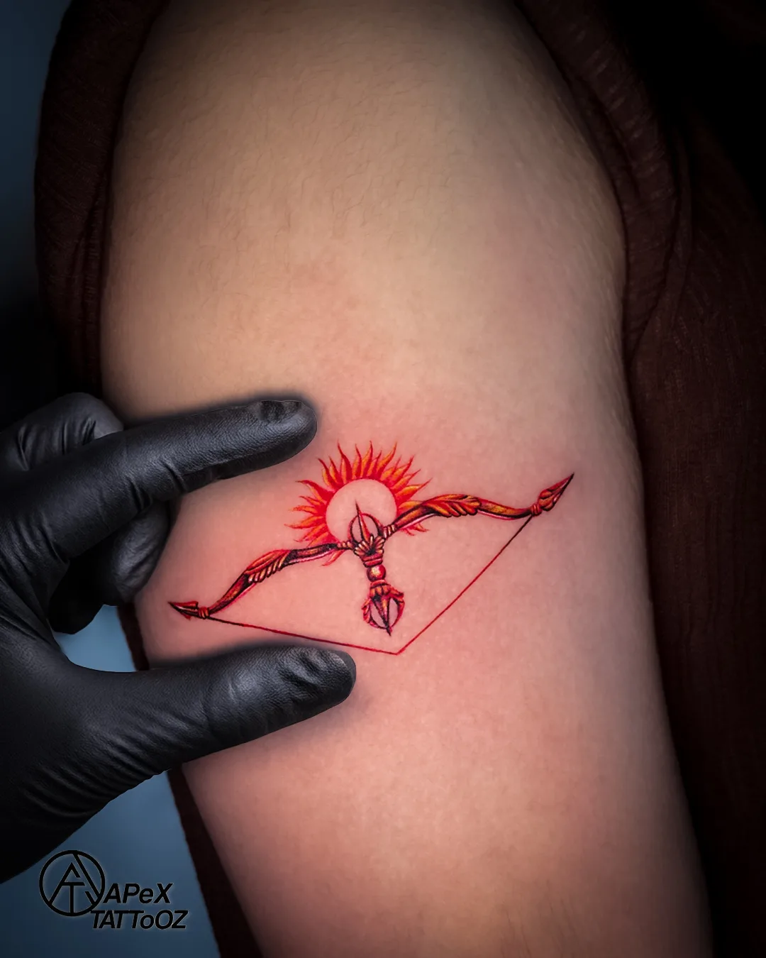 Small colour bow-and-arrow upper-arm tattoo by Apex Tattooz Delhi