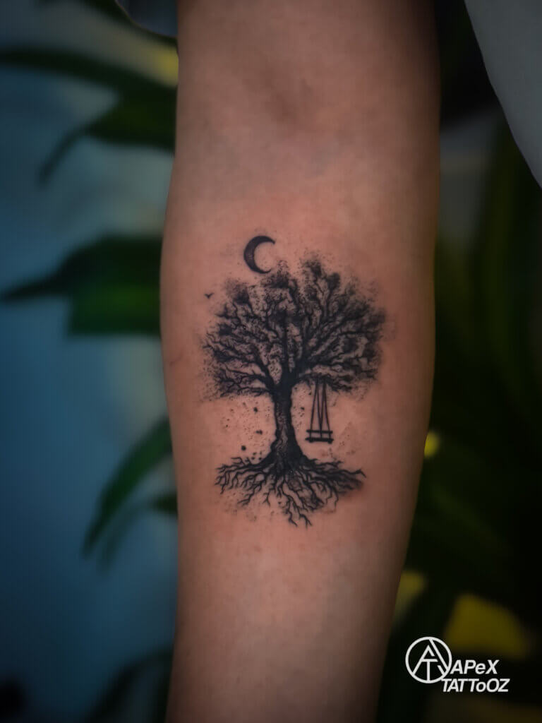 Black-and-grey tree tattoo with a hanging swing, crescent moon and visible roots