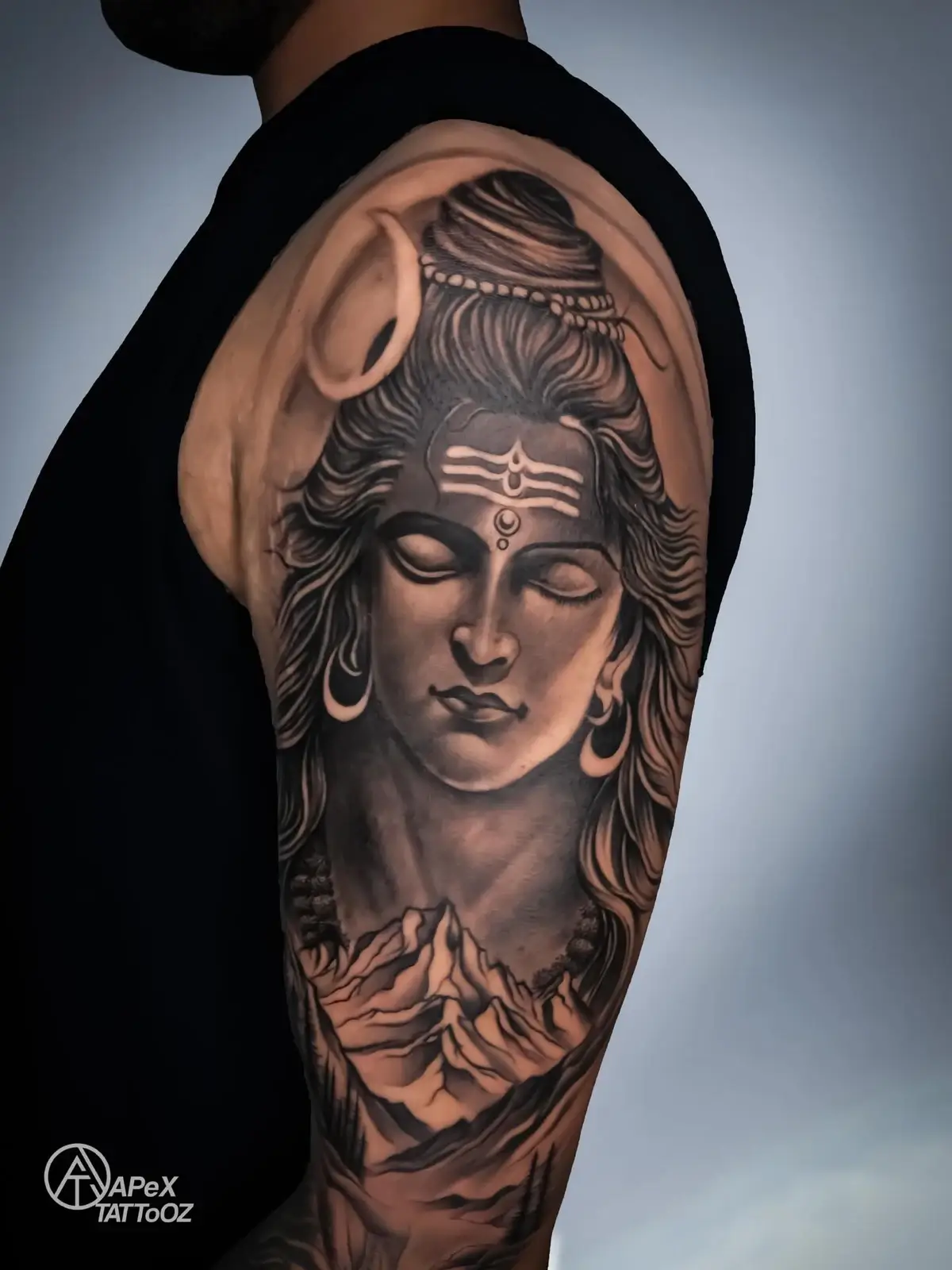 A Shiva portrait above a mountain landscape on the upper arm.
