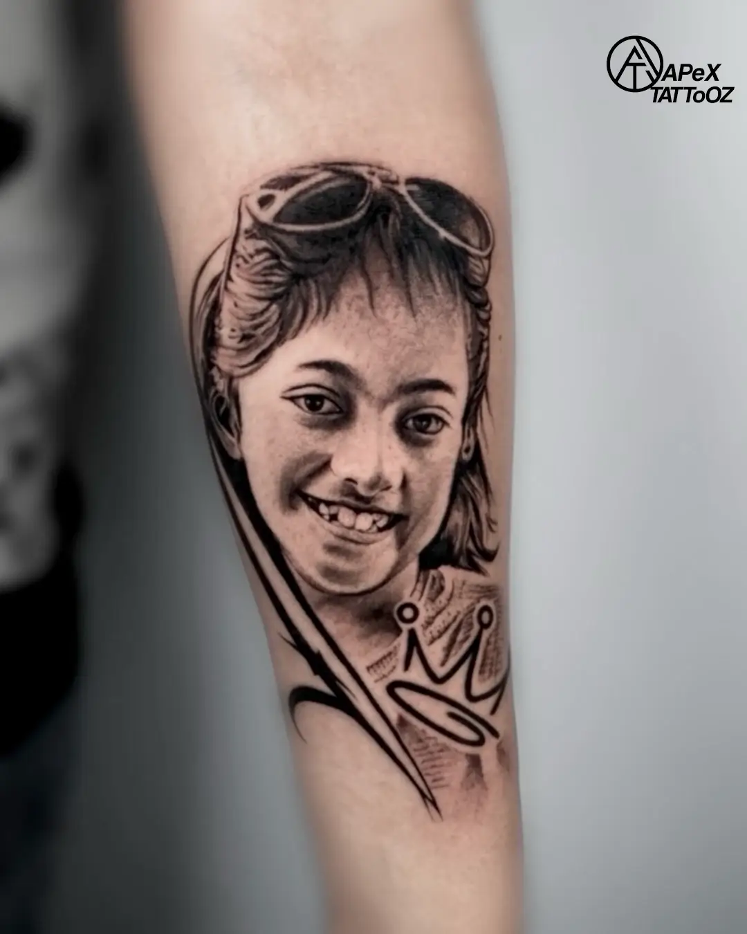A smiling portrait with sunglasses and a crown on the forearm.