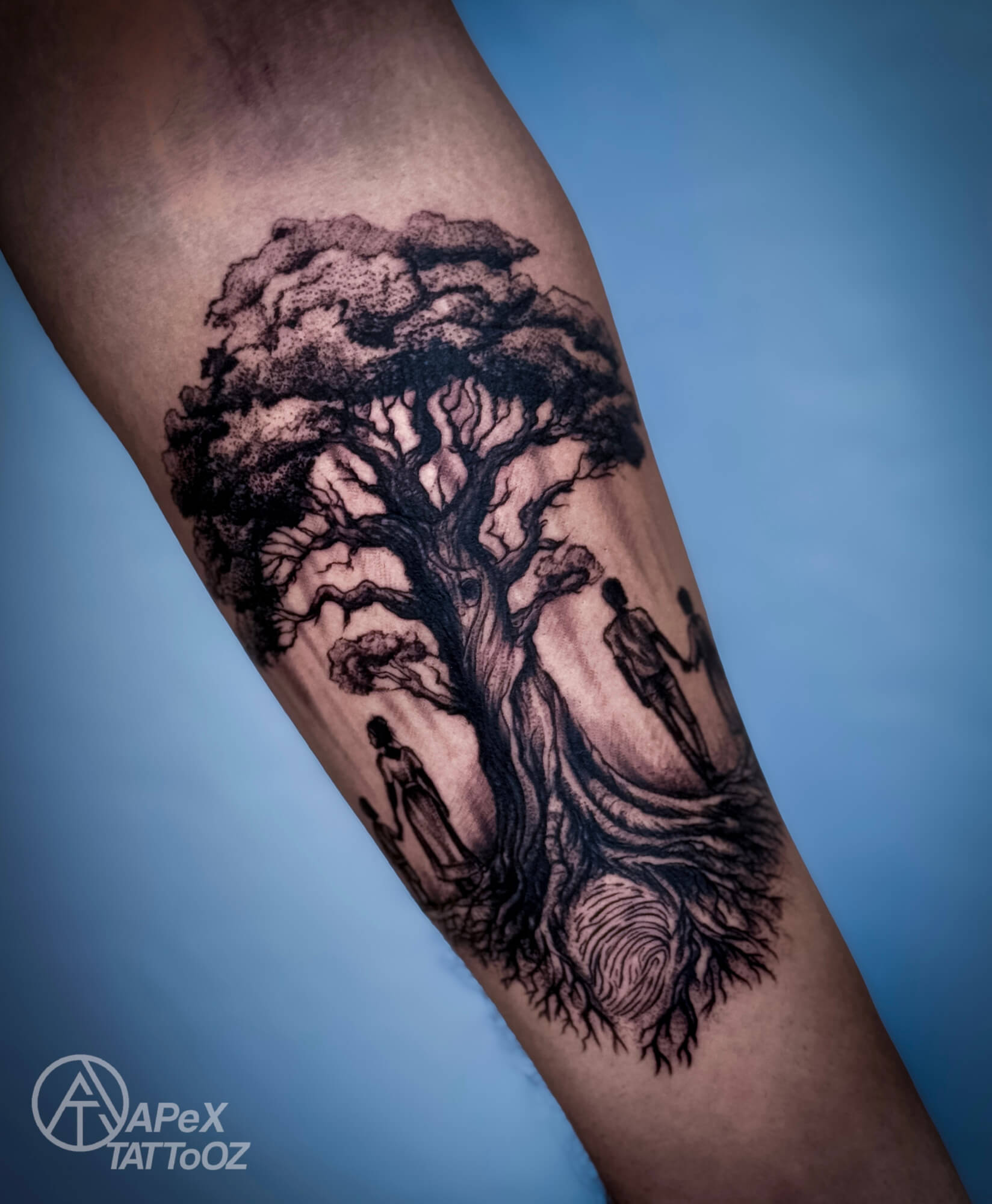 Tree tattoo with small figures beside the trunk and a fingerprint enclosed by the roots