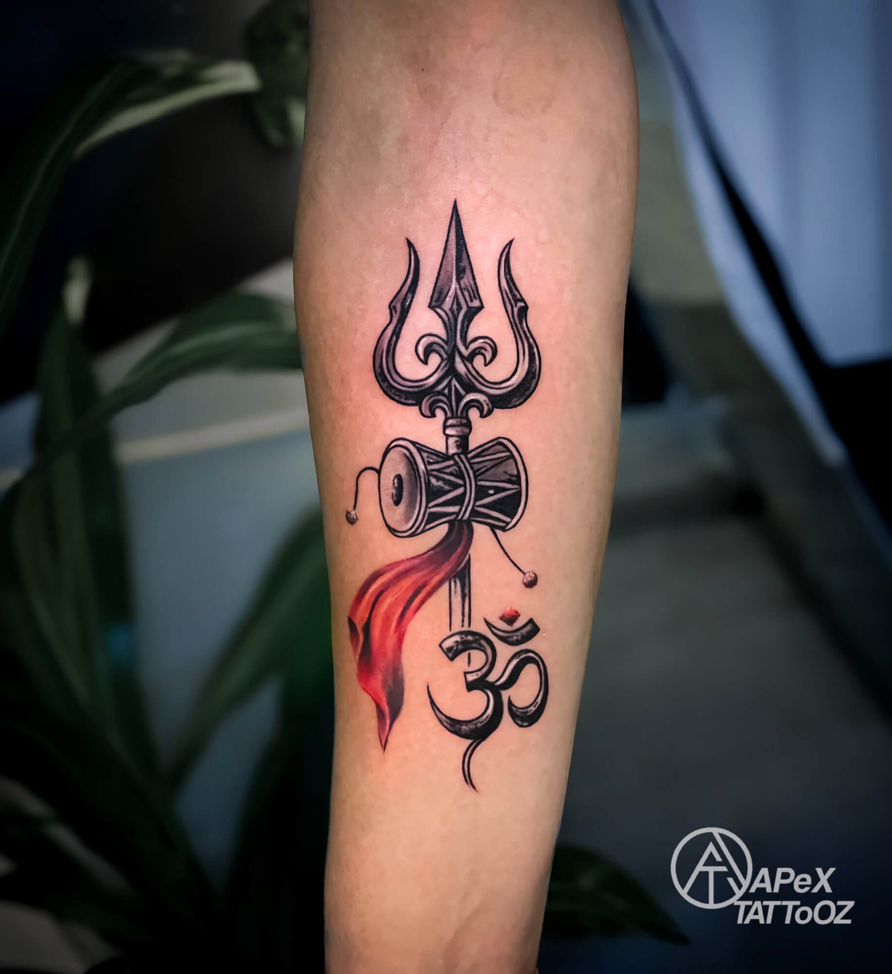 Trident and damru tattoo above an Om symbol, with red-orange cloth detail on the forearm
